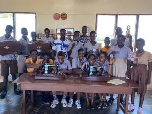 a crowd of students stand and sit behind a table that has 2 sewing machines on it
